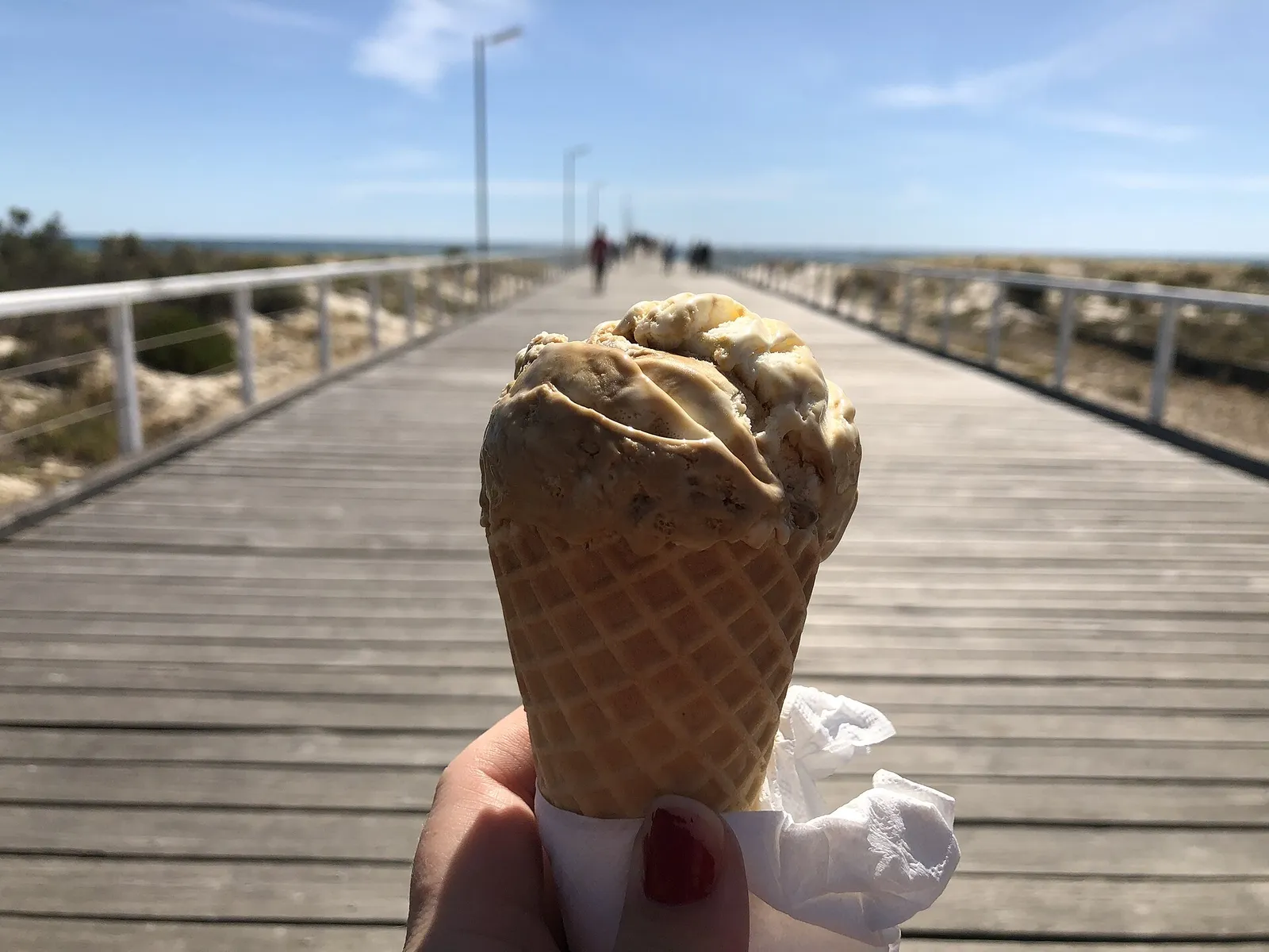 An ice cream cone held up on a boardwalk. The photo was not taken in Columbus.