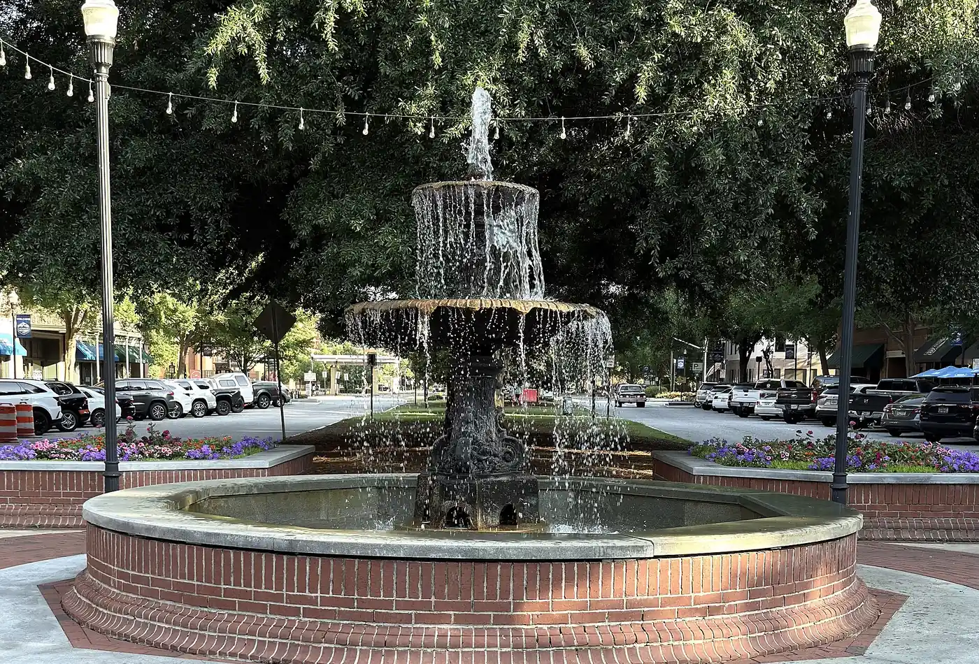 A fountain in the median of Broadway in Uptown Columbus, under string lights and live oaks.